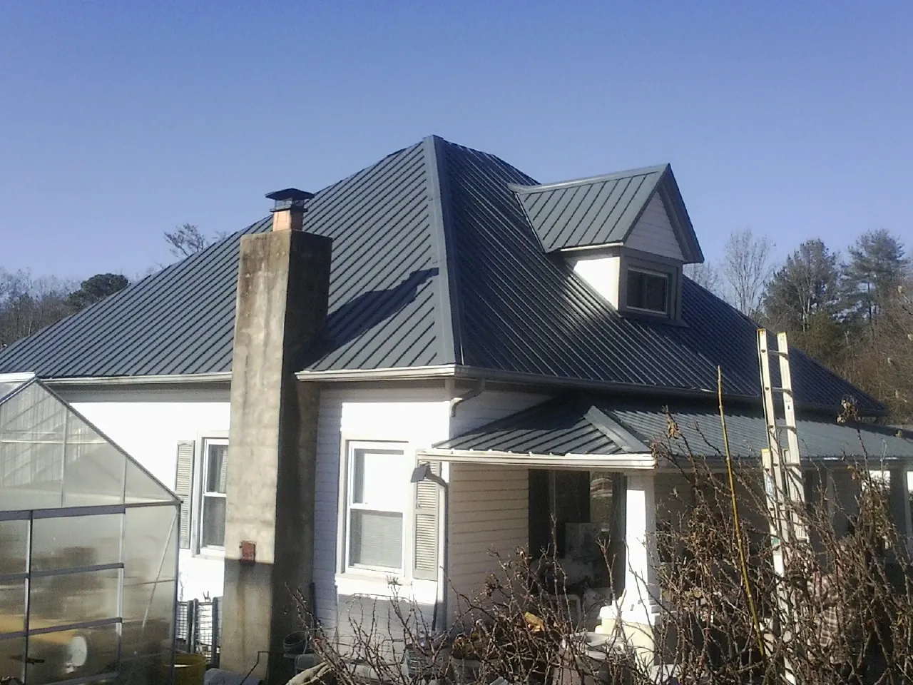 Dark blue standing seam metal roof on a white farmhouse with dormer — Slate & Tile Roof Repair by Roofing Brothers in Lorraine