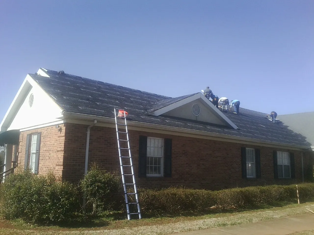 Crew tearing shingles off a brick ranch roof with a ladder set — Metal Roof Repair work by our crew in Lorraine