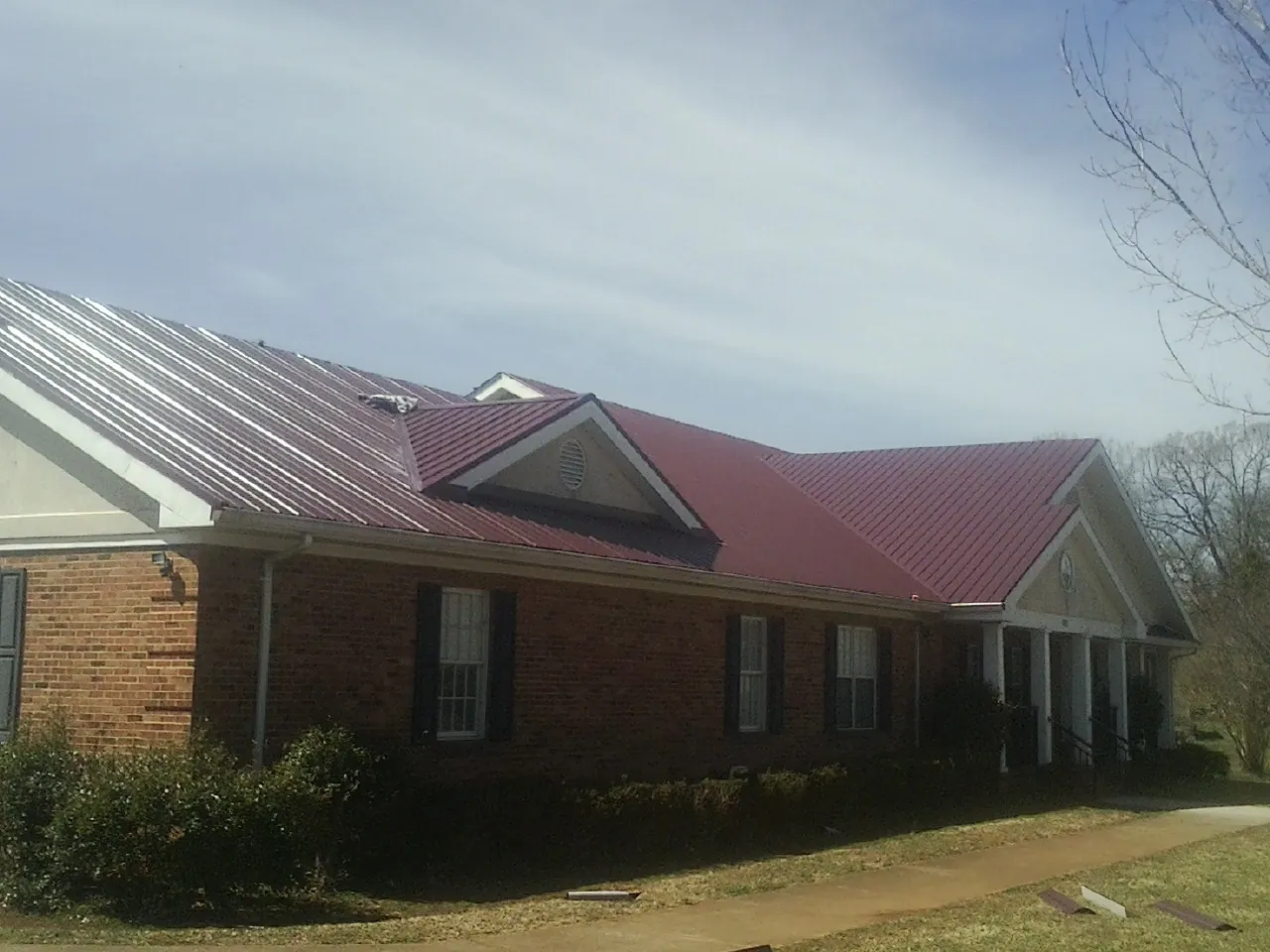 Red metal roof with gabled entries on a long brick building, from a Hail Damage Roof Repair job in Lorraine