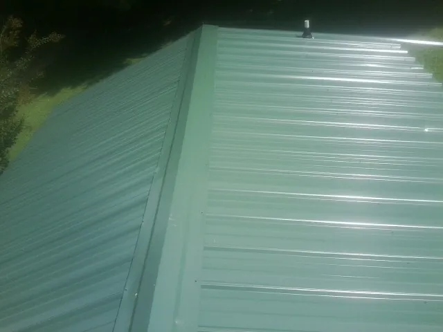 New green metal panels meeting at the ridge of a roof — Flat Roof Repair work by our crew in Lorraine