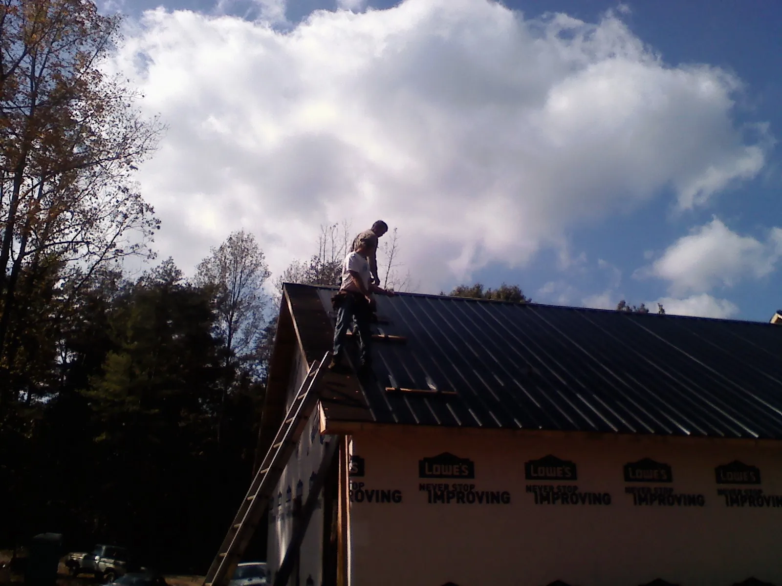 Roofer fastening dark metal panels high against a cloudy sky, from a Roof Inspection job in Lorraine