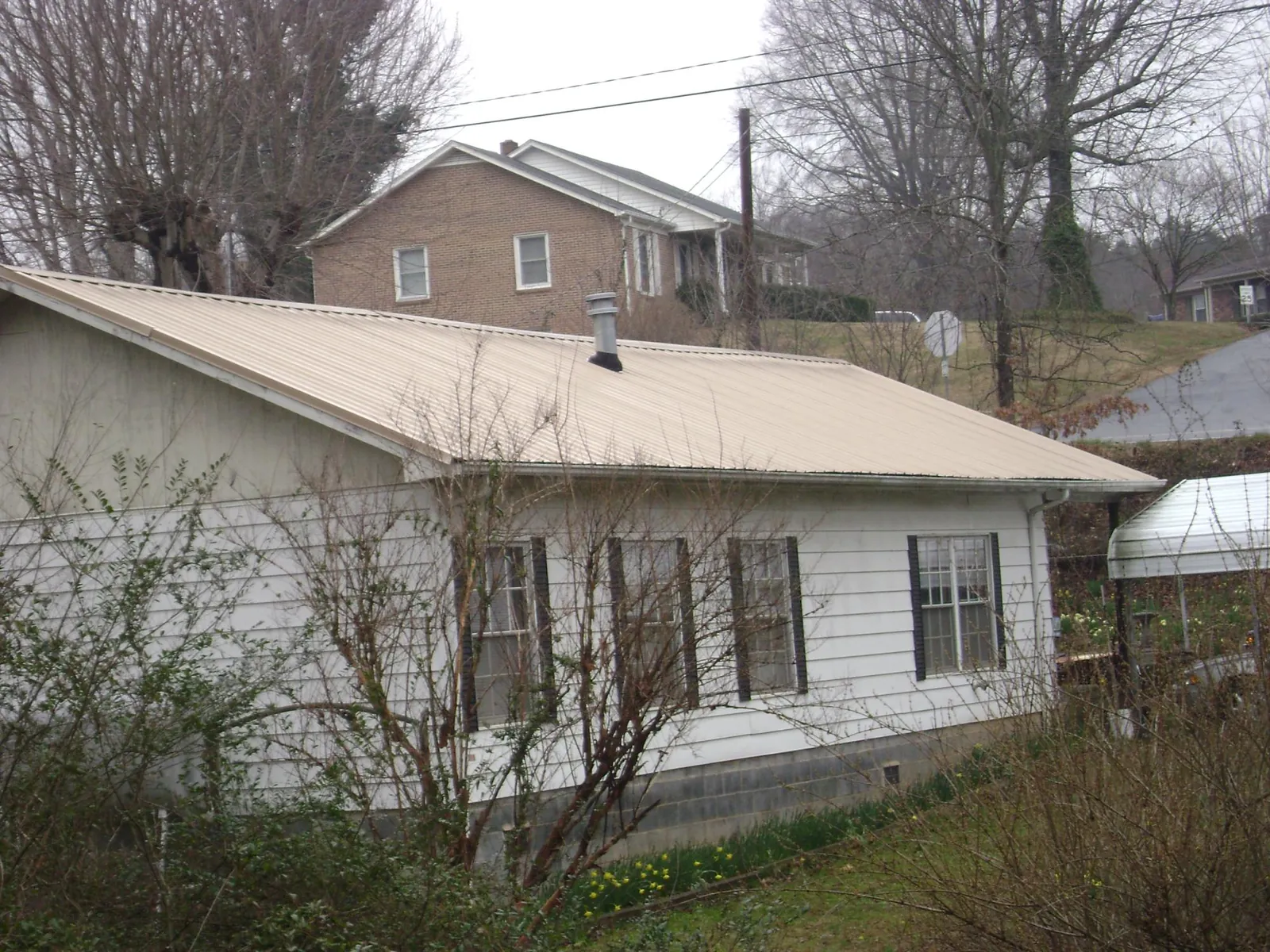 Tan metal roof on a white sided house set into a hillside — Commercial Roofing by Roofing Brothers in Lorraine